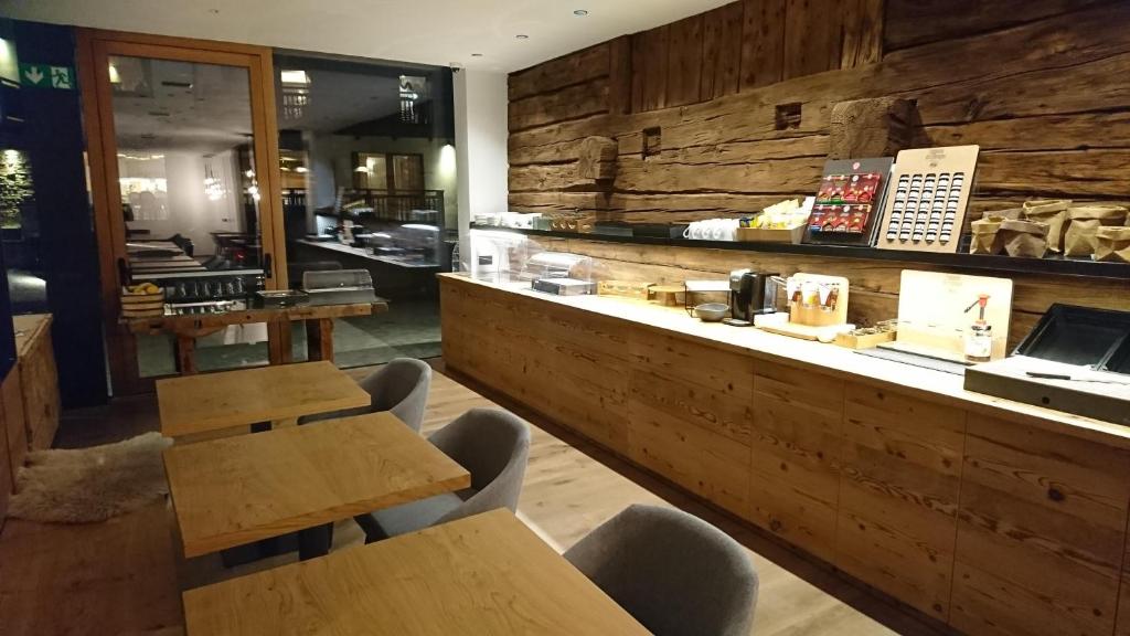 Mūsdienīga kafejnīca ar koka mēbelēm un siltu gaisotni, kurā redzami galdi un bufete ar dzērieniem un uzkodām.