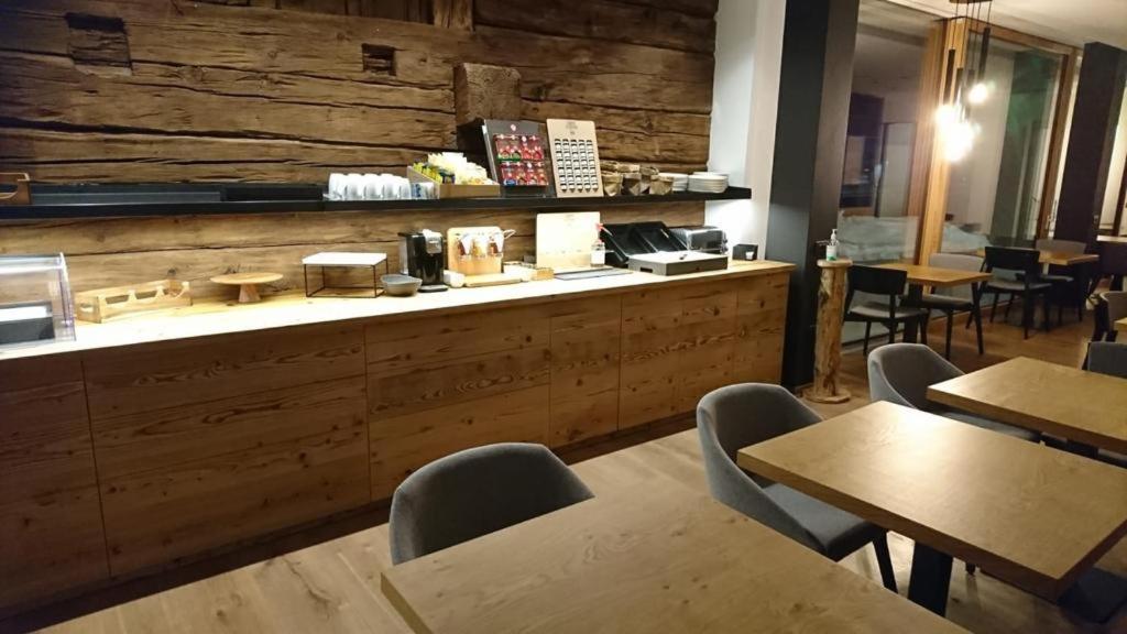 Mūsdienīgs restorāna interjers ar koka elementiem, kurā redzama gaumīga apkalpošanas zona un ēdamgaldi. Dabiskais apgaismojums rada patīkamu atmosfēru.