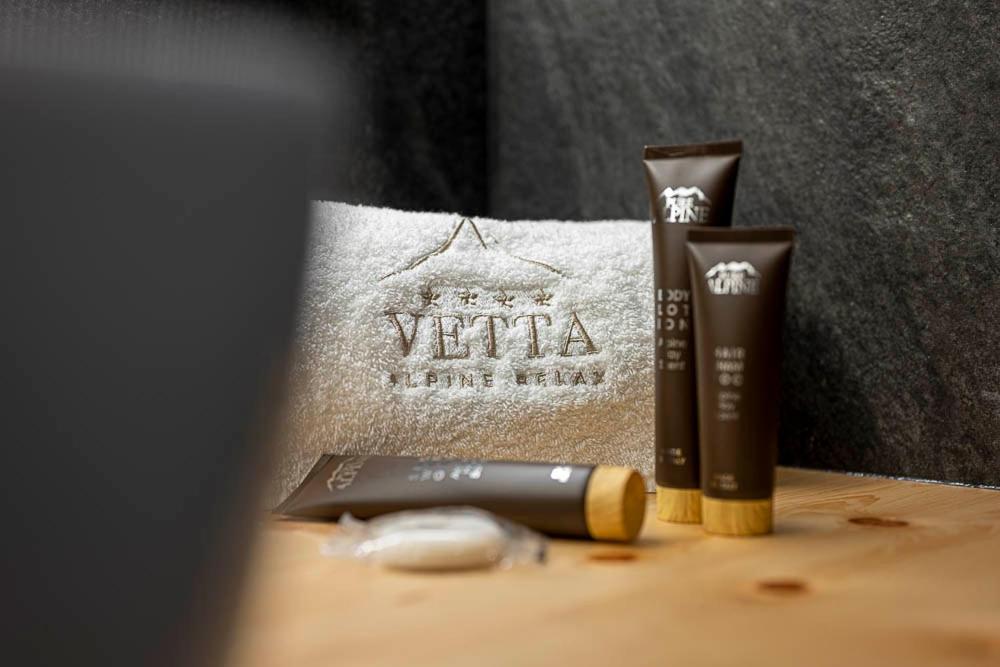 VETTA Alpine Relax zīmola kosmētikas komplekts ar trīs krēmiem un dvieli, kas rotāts ar logotipu, uz koka virsmas.