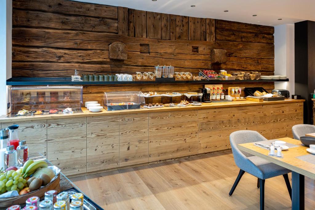 Kafejnīca ar siltu koka apdari un elegantu interjeru, kurā redzama dažādu uzkodu un dzērienu izvēle. Uz galda atrodas augļi un galda piederumi, radot patīkamu atmosfēru.