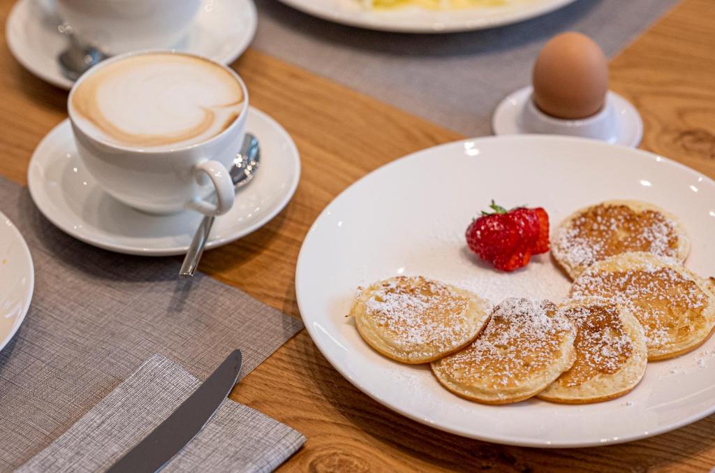 Broka, kas sastāv no pankūkām ar pūdercukuru, zemeņu un vārīta ola, kopā ar krūzi latte. Ideāls rīts ar gardu brokastu komplektu.