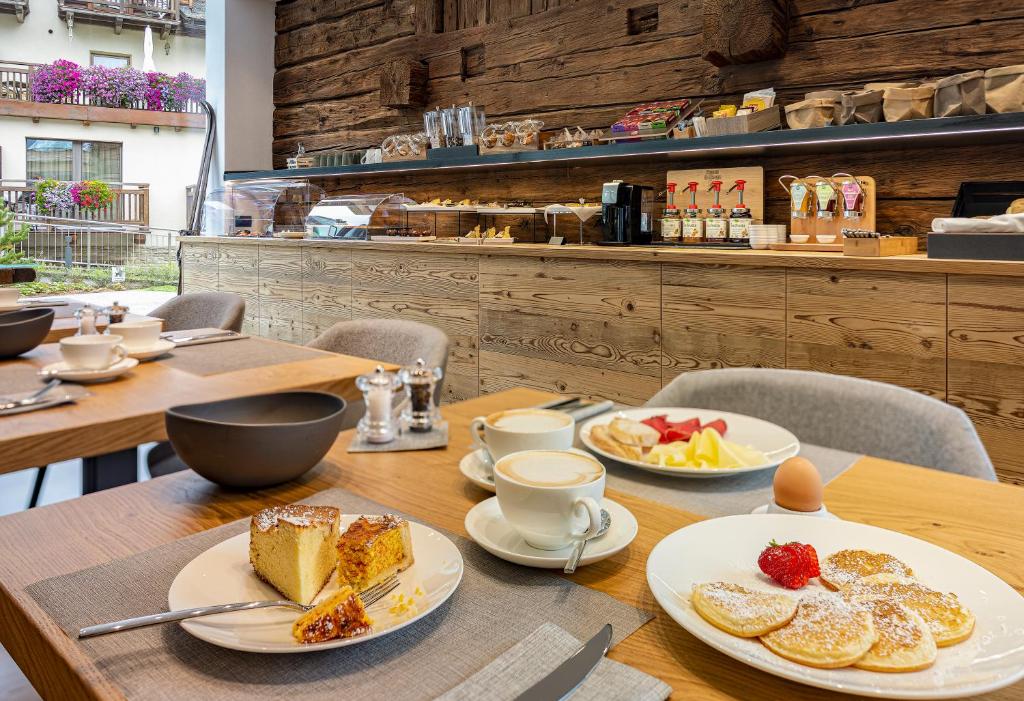 Brokastis ar gardām pankūkām, kūkām un kafiju modernā un mājīgā kafejnīcā ar koka interjeru. Uz galda ir dažādi ēdieni un dzērieni, radot patīkamu atmosfēru.