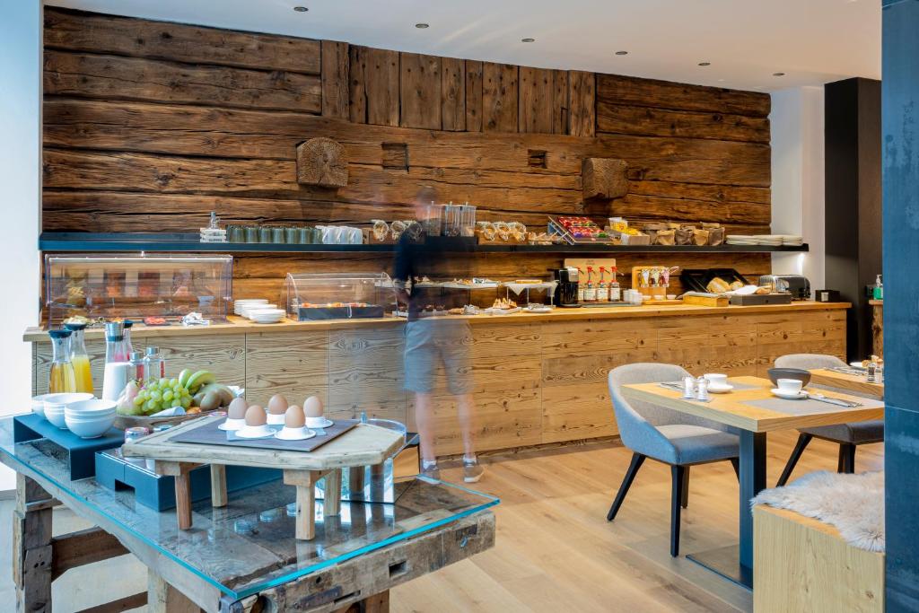 Mūsdienīga brokastu zona ar koka apdari, kurā redzams ēdienu klāsts un dzērienu izvēle, kā arī eleganti galdi un krēsli.