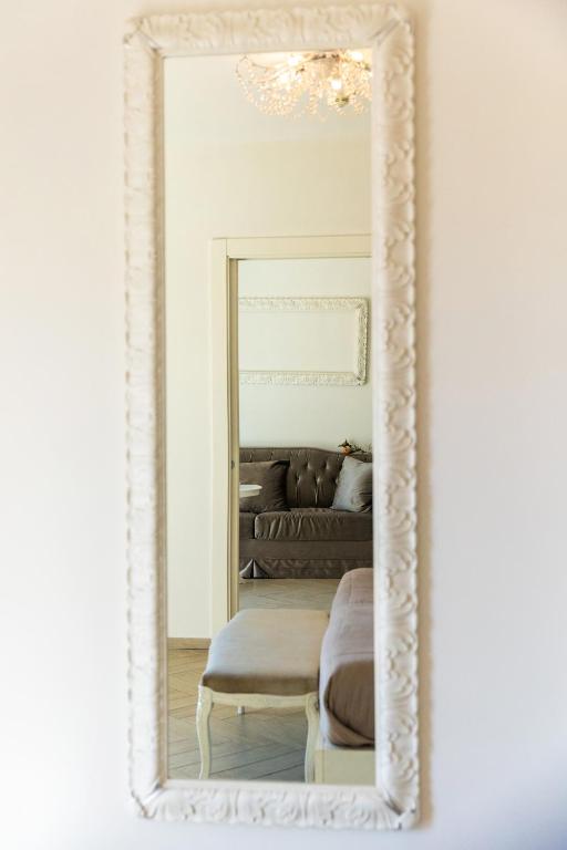 Elegants garš spogulis ar izsmalcinātu rāmīti, atspoguļojot stilīgu viesistabu ar dīvānu un dekoratīviem elementiem.