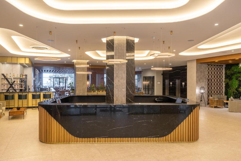 Mūsdienīgs viesnīcas reģistratūras izskats ar melnu marmora letīti un modernu apgaismojumu, kas rada elegantu atmosfēru. Interjerā ir redzamas siltas krāsas un augu elementu dekorācijas.