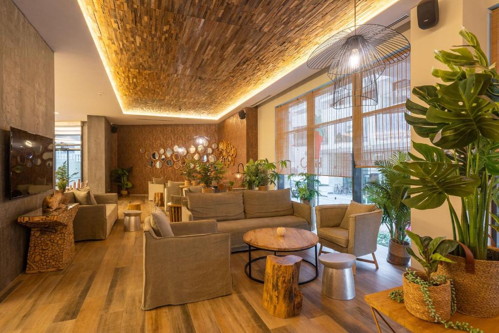 Mūsdienīgs un elegants viesnīcas vestibils ar koka griestiem, ērtām mēbelēm un zaļām augiem, kas rada siltu un viesmīlīgu atmosfēru.