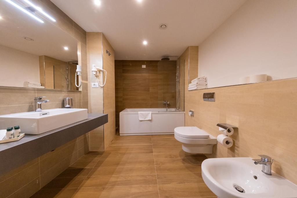 Mūsdienīgs vannas istabas interjers ar koka grīdu, elegantu izlietni un vannu. Telpas apgaismojums rada patīkamu atmosfēru.