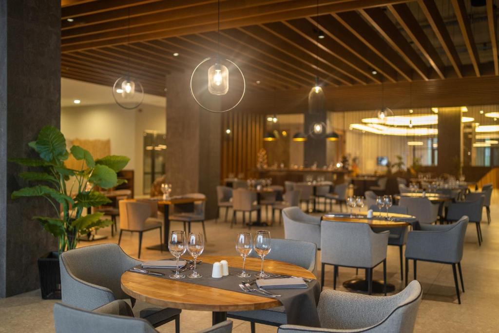 Moderns restorāns ar elegantiem galdiem un krēsliem, kurās ir glāzes un galda piederumi, radot stilīgu un aicinošu atmosfēru. Dekorā ir izmantoti koka elementi un zaļumi, kas piešķir dzīvīgumu.