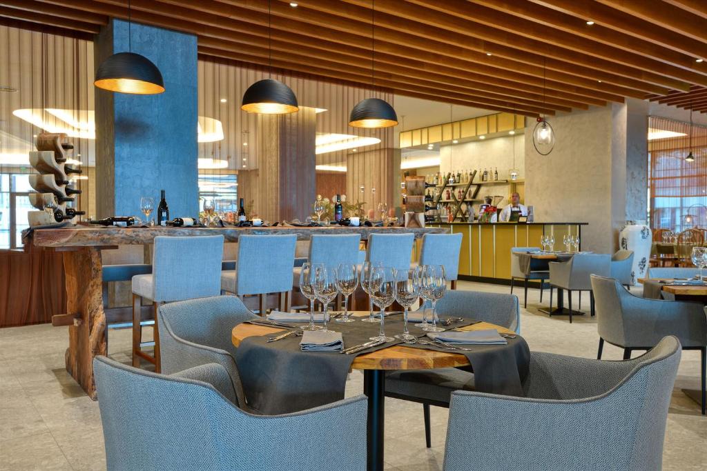 Mūsdienīgs restorāna interjers ar elegantiem galdiem, krēsliem un plašu bāru, kas piedāvā plašu dzērienu izvēli. Atmosfēra ir gaisīga un aicinoša, ideāla maltītēm un socializācijai.