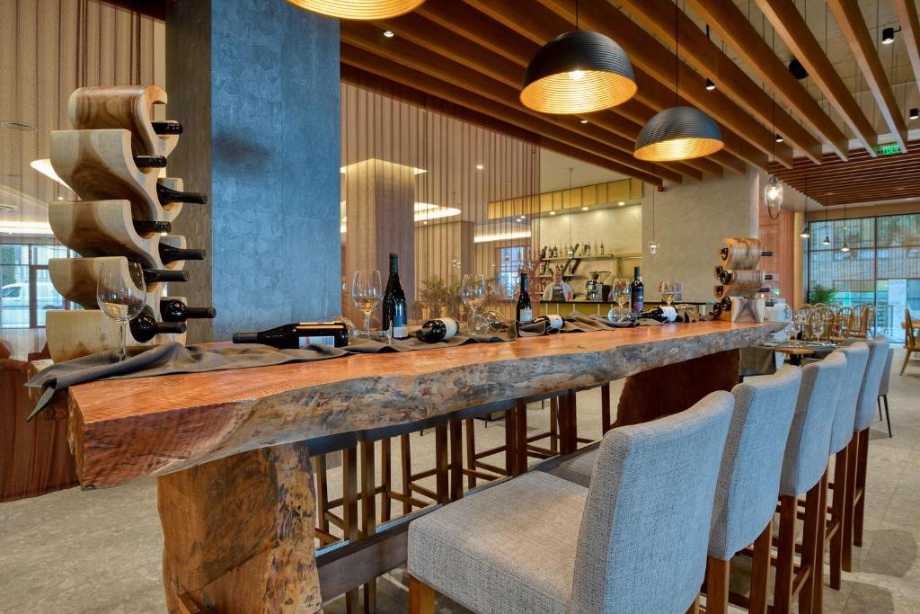 Mūsdienīgs bārs ar elegantu koka galdu, stikla glāzēm un vīna pudelēm, kas izkārtotas uz galda, un stilīgu interjeru, kas apvieno koka un akmens elementus.