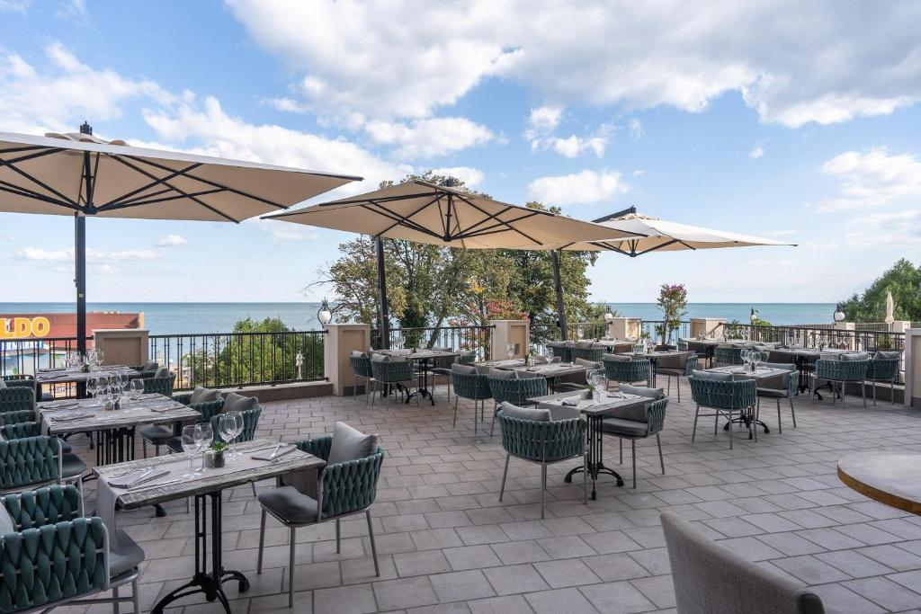 Terase pie jūras ar ērtām galdiem un saulessargiem, ideāla vieta relaksācijai un maltītēm brīvā dabā. Skaists skats uz ūdeni un zaļo apkārtni.