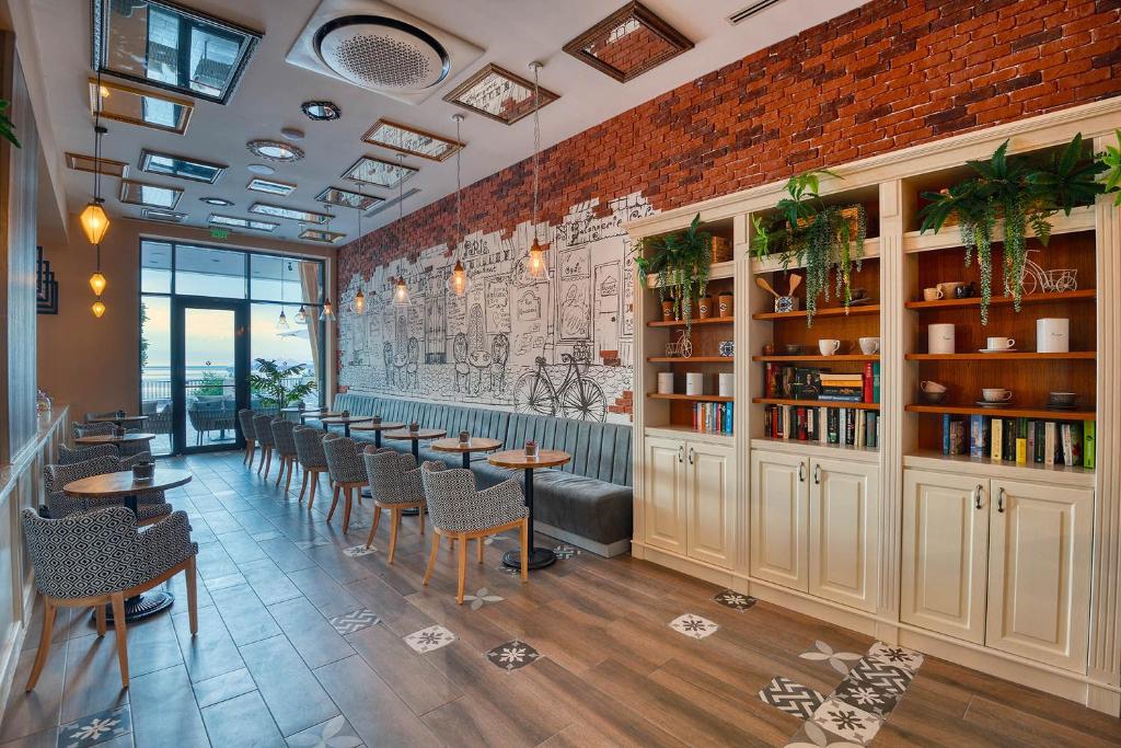 Mūsdienīga kafejnīca ar siltu interjeru, kas apvieno ķieģeļu sienas, augu dekorus un komfortablas sēdvietas. Gaisma ieplūst no lielajiem logiem, radot patīkamu atmosfēru.