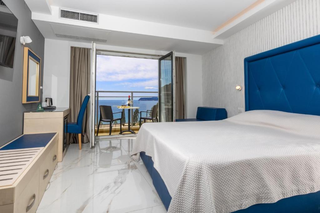 Mūsdienīga viesnīcas numura interjers ar skatu uz jūru. Numurā ir zilas krāsas gulta, rakstāmgalds un balkons ar ērtām mēbelēm.