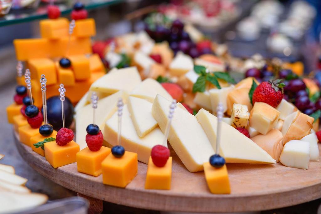 Siera šķēļu un augļu šķīvis ar dažādu sieru, ogu un augļu kompozīciju, kas pasniegts uz koka pamatnes.