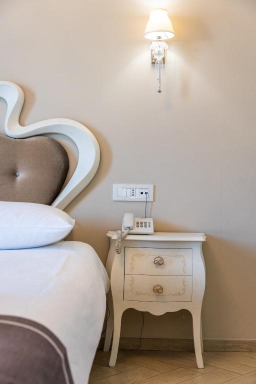 Gultas blakus esošais naktsgaldiņš ar tālruņa aparātu un stilīgu apgaismojumu, radot mājīgu atmosfēru.