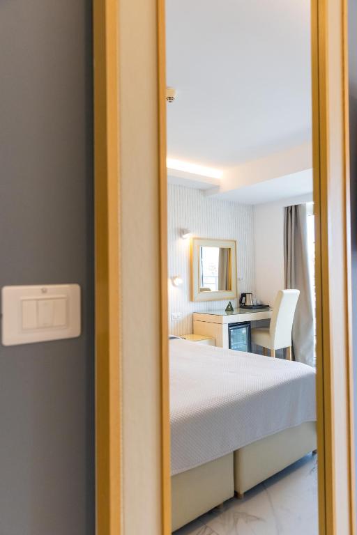 Modernas guļamistabas interjers ar gultu un darba zonu, redzams caur atvērta durvju rāmja spoguli. Svaiga un gaiša atmosfēra ar neitrālām krāsām.