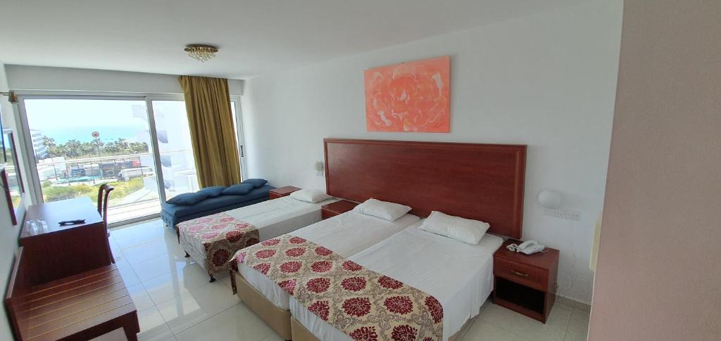 Gaiša viesnīcas istaba ar divām gultām, dīvānu un skatu uz āru. Istabā ir moderns interjers un liels logs ar daudz gaismas.