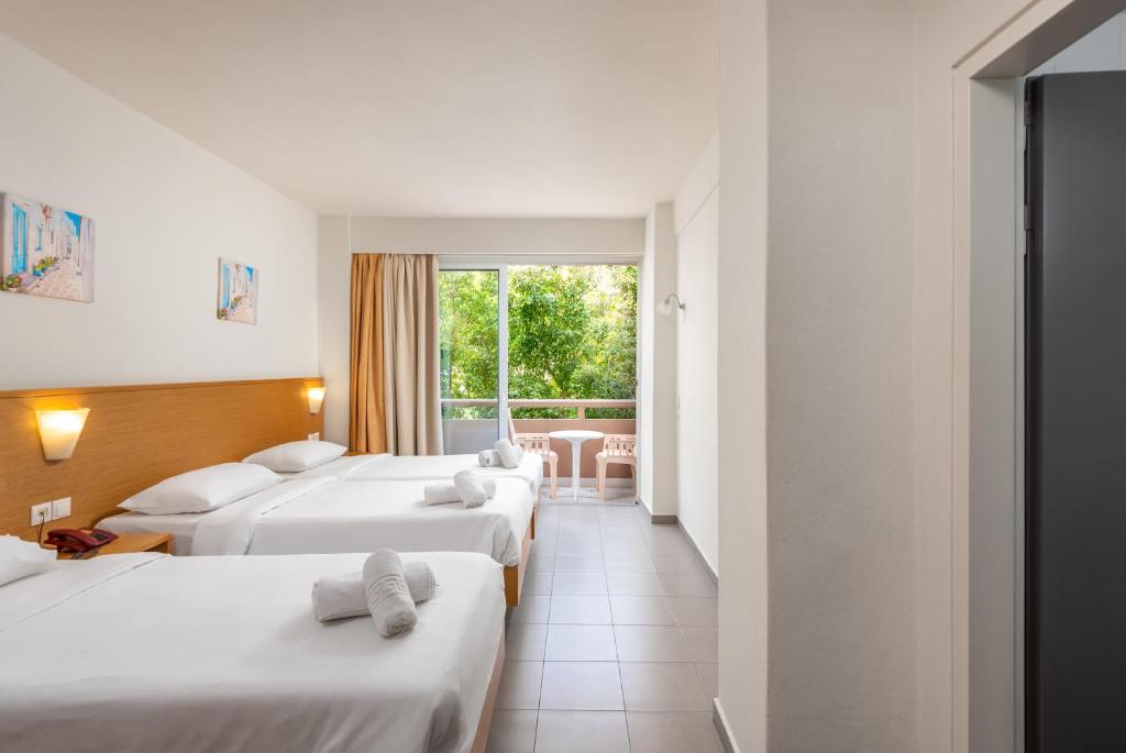 Mūsdienīgs viesnīcas numurs ar divām gultām, baltiem veļas izstrādājumiem un balkonā esošiem krēsliem. Logi nodrošina skatu uz zaļo dabu.