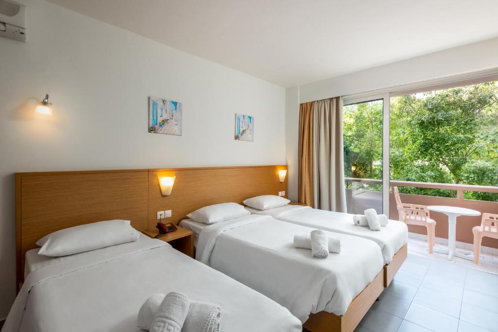 Gaiša viesnīcas numuriņa interjers ar trim gultām, mīkstiem dvieļiem un skatu uz dārzu. Numurā ir gaismas avoti un balkons ar āra mēbelēm.