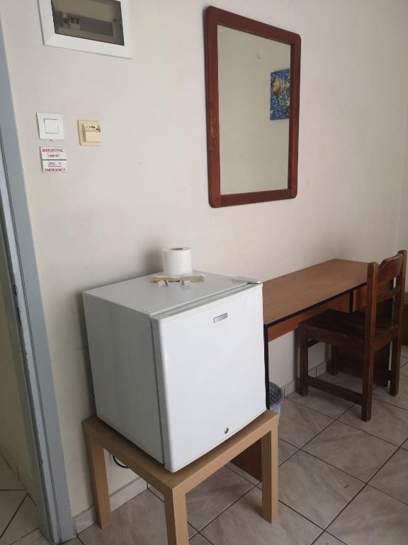 Baltā ledusskapja un koka galda kombinācija ar krēslu un spoguli pie sienas, radot vienkāršu un funkcionālu telpu.