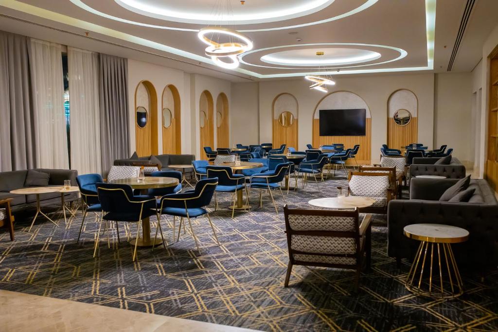 Mūsdienīgs atpūtas telpa ar stilīgām zilām krēslām, elegantiem galdiem un gaismas elementiem, radot komfortablu un viesmīlīgu atmosfēru.