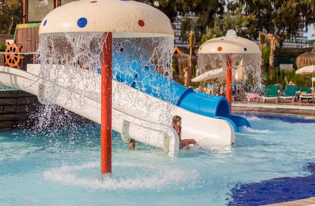 Aqua parka slidkalni ar ūdens strūklām un bērniem, kas priecājas par peldēšanu. Vasaras izklaides un atpūtas vieta, kas piedāvā jautrību un relaksāciju.