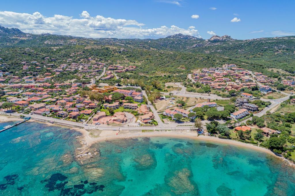 Aerial view of a coastal village featuring colorful homes and green hills, with a clear turquoise sea in the foreground. This serene landscape highlights the beauty of the Mediterranean coastline.