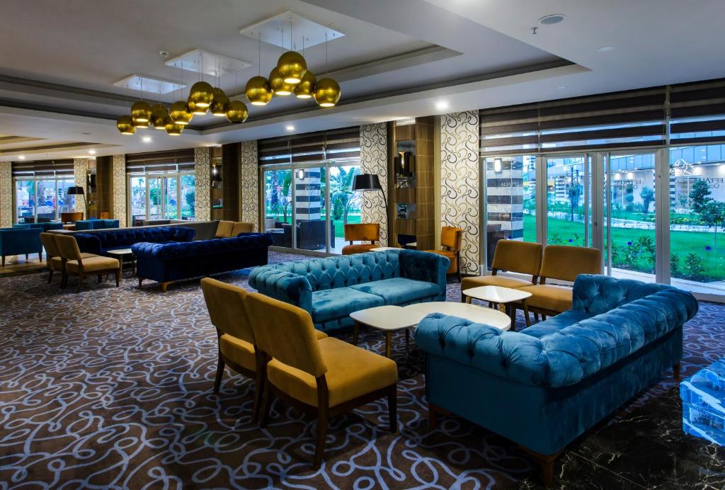 Mūsdienīgs viesnīcas interjers ar zilu dīvānu un gaišām mēbelēm, kas rada elegantu un komfortablu atmosfēru. Labi apgaismots telpas dizains, kas iekļauj lielus logus un zaļo vidi ārpusē.