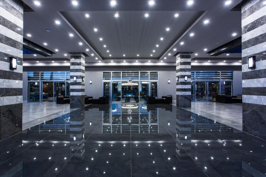 Mūsdienīgs viesnīcas vestibils ar elegantu apgaismojumu un spīdīgām grīdām, kas atspoguļo telpas dizainu. Stilīgi akmens stabi un ērti sēdvietas rada viesmīlīgu atmosfēru.