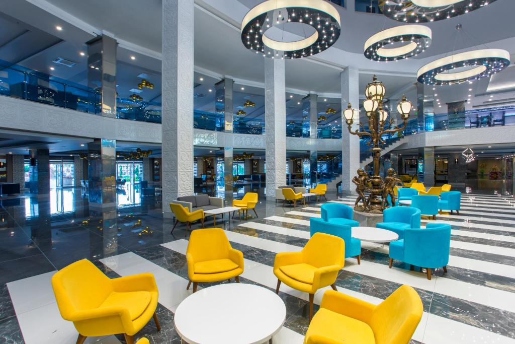 Mūsdienīga viesnīcas iekštelpa ar stilīgām dzeltenām un zilo krēslu grupām, apgaismojumu un elegantiem elementiem. Interjers izceļas ar elegantu dizainu un plašumu, radot patīkamu atmosfēru.