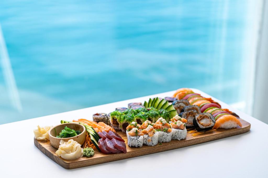 Svaigu suši šķīvītis ar dažādiem suši veidiem, garnelēm, dārzeņiem un garšvielām, pasniegts uz koka dēļa ar okeāna fonu.