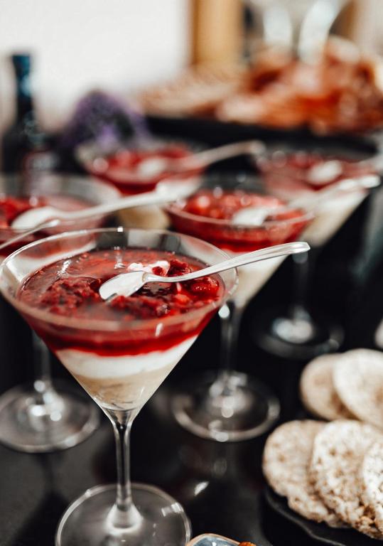 Salds deserts ar ogu mērci un krējuma slāni, pasniegti elegantiem martini glāzēs. Fonā redzami grauzdiņi un citi uzkodu elementi.