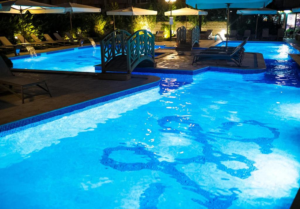 Zilā baseina zona ar tiltiņu un saulessargiem, apgaismota naktī, radot relaksējošu atmosfēru. Ideāla vieta atpūtai un izklaidei.