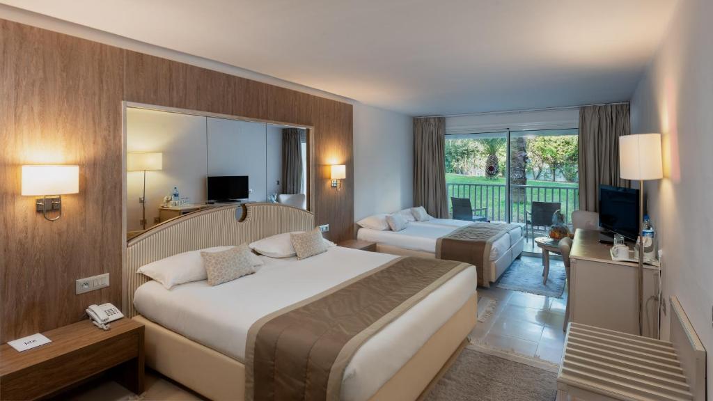 Mūsdienīgs viesnīcas numurs ar divām gultām, dīvānu un lielu logu, caur kuru redzams dārza skats. Interjers ir gaišs un ērts, ar koka akcentiem un modernām iekārtām.