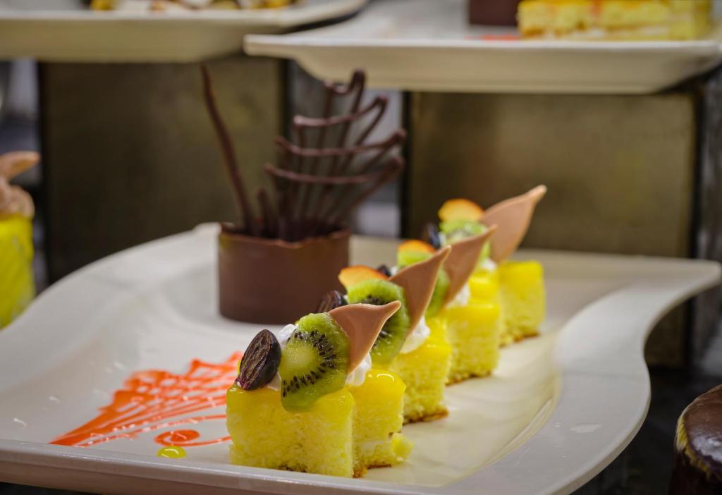 Saldējumā redzami krāsaini deserti, ieskaitot dzeltenas kūkas ar augļiem un šokolādes dekoriem. Estētiski noformēti saldumi ir lielisks kārdinājums.