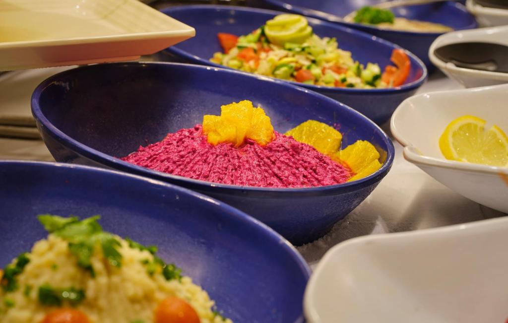 Skaisti pasniegti ēdieni dažādās bļodās, ieskaitot rozā biezeni ar apelsīnu šķēlēm un dārzeņu salātus.