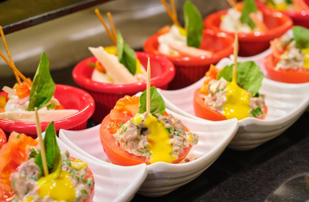Tomātu uzkodas ar dažādām pildījumu kombinācijām, dekorētas ar zaļumiem un zobu bakstāmiem. Izsmalcināta un krāsaina ēdiena prezentācija.