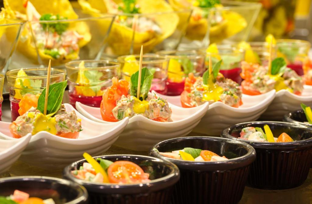 Dažādu gaumīgu uzkodu izkārtojums, ieskaitot salātus un dārzeņu porcijas, pasniegtas elegantos traukos. Izskatās, ka šie ēdieni ir ideāli piemēroti svinībām vai svētku pasākumiem.