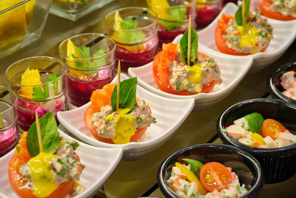 Skaisti pasniegti uzkodu šķīvji ar dažādiem dārzeņu un jūras velšu salātiem, papildināti ar krāsainiem desertiem glāzēs.