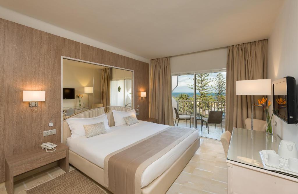 Mūsdienīga viesnīcas istaba ar plašu gultu, rakstāmgaldu un balkonu, no kura paveras skats uz jūru. Interjers ir gaišs un elegants, ar dabīgām koka un neitrālām krāsām.