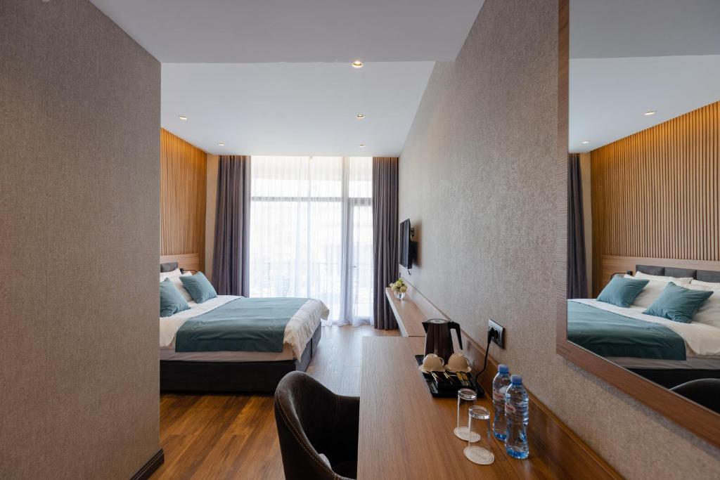 Mūsdienīgs viesnīcas numurs ar gultu, darba galdu un plašu logu, caur kuru ieplūst dabiska gaisma. Interjers ir elegants ar koka akcentiem un neitrālām krāsām.