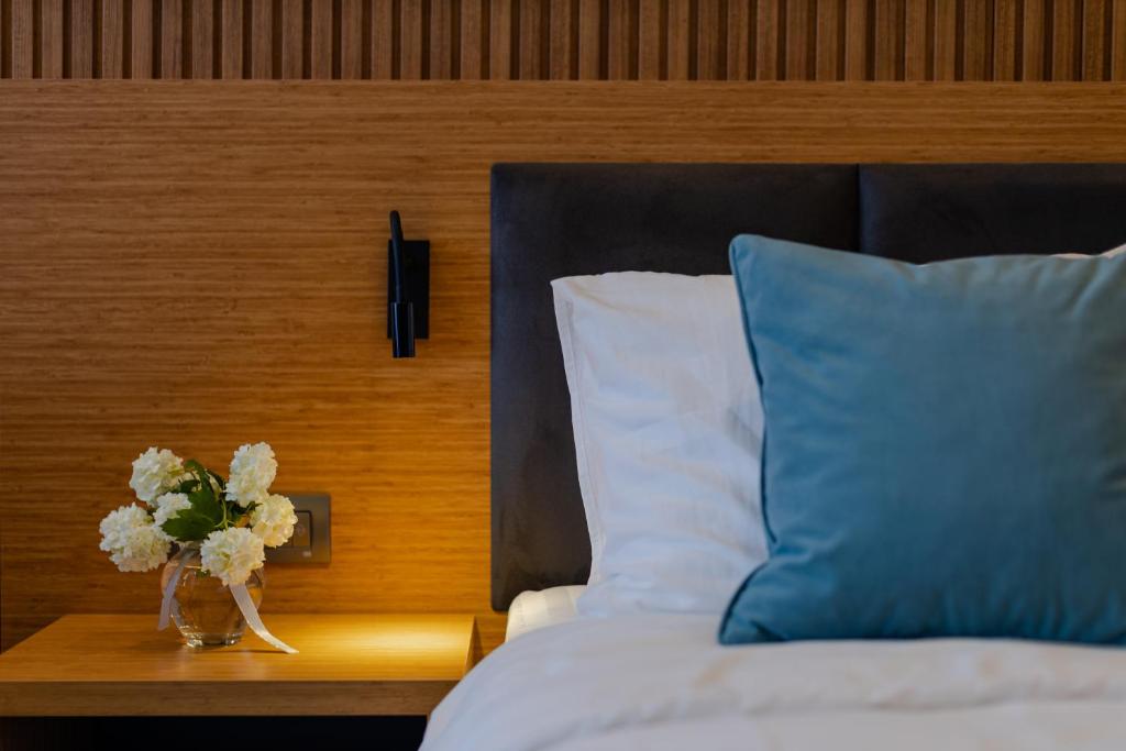 Mūsdienīgs guļamistabas interjers ar elegantu gultu, spilvenu un ziedu kompozīciju uz naktsgaldiņa. Siltas koka toņu akcenti rada mājīgu atmosfēru.