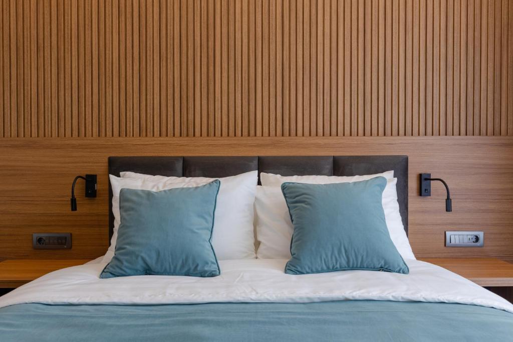 Mūsdienīgs guļamistabas interjers ar koka apdari, gaišu gultu un divām zilo spilveniem uz gultas.