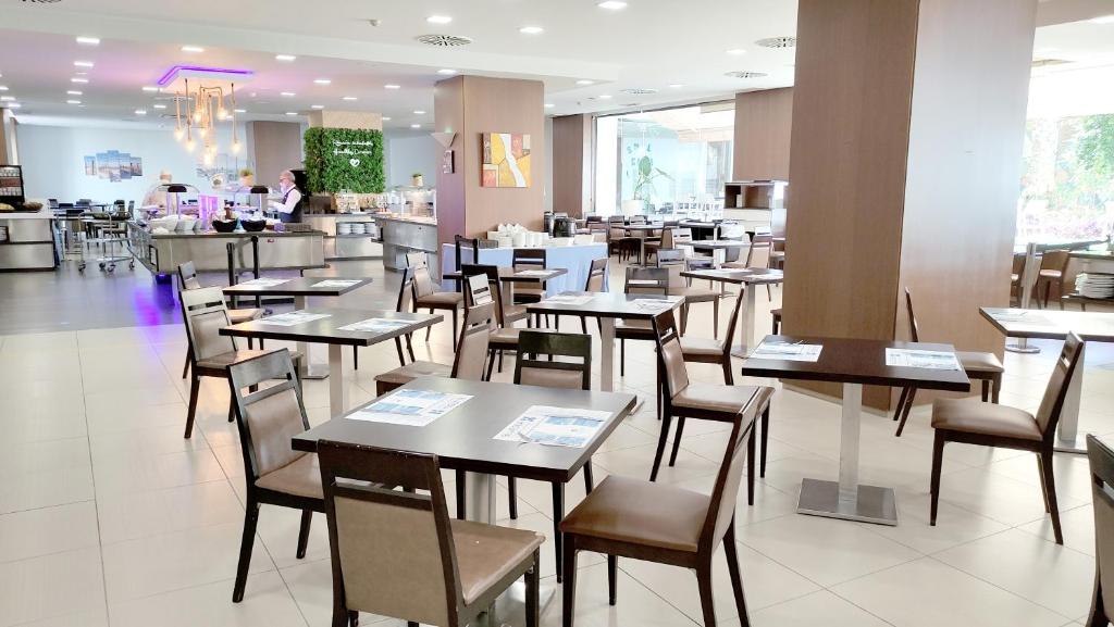 Mūsdienīgs restorāns ar ērtām galdiem un krēsliem, kur ir redzama bufete un apkalpojošais personāls. Gaisma un interjers rada patīkamu atmosfēru.