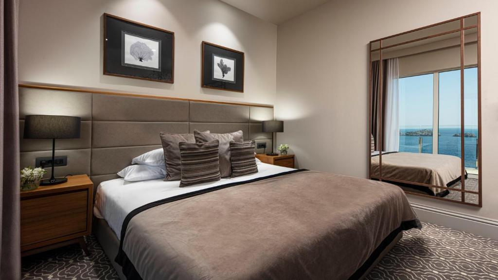 Mūsdienīgs guļamistabas interjers ar skatu uz jūru, kurā ir ērta gulta un eleganti dekori, kā arī liels spogulis. Ideāla vieta atpūtai un relaksācijai.