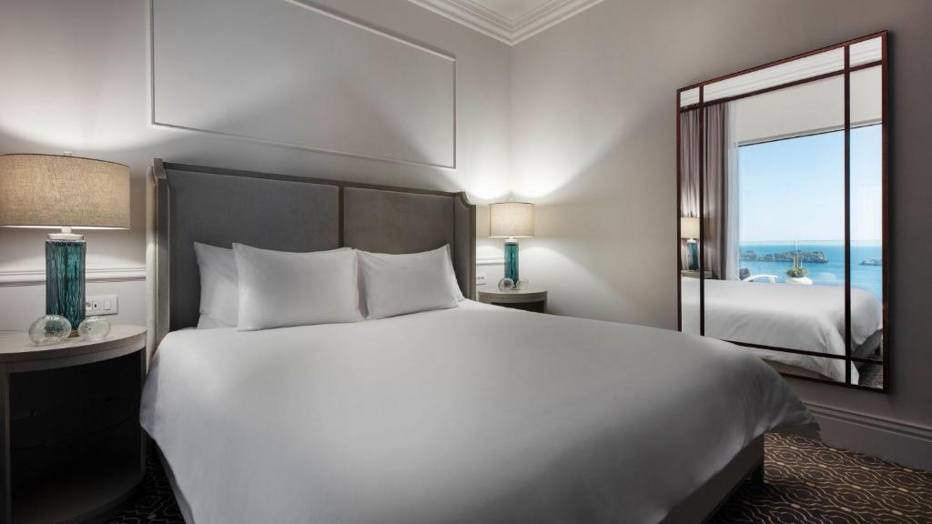 Mūsdienīgs guļamistabas interjers ar ērtu gultu, lampu un skatu uz jūru caur spoguli.