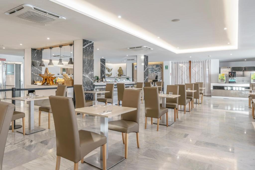 Moderns restorāns ar elegantiem galdiem un krēsliem, kas rada patīkamu atmosfēru. Interjerā redzami marmora elementi un gaiša apgaismojuma dizains.