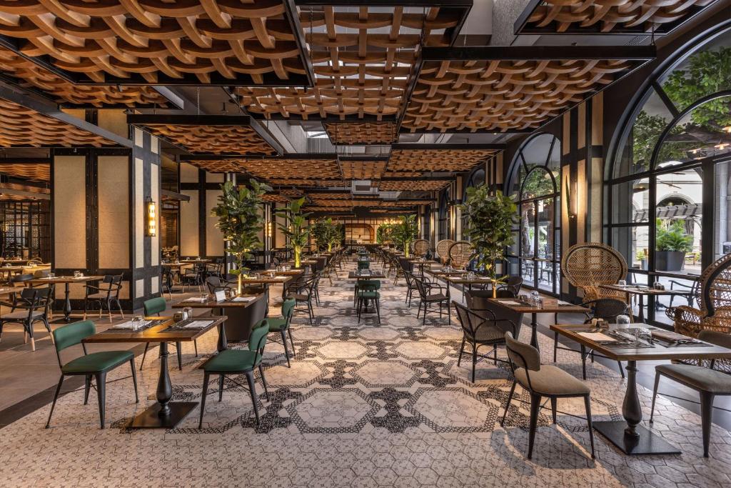 Elegants restorāns ar modernu interjeru, kurā ir koka griesti un plaši logi, kas piedāvā dabisko apgaismojumu. Mūsdienīgas mēbeles un zaļumi rada patīkamu atmosfēru.