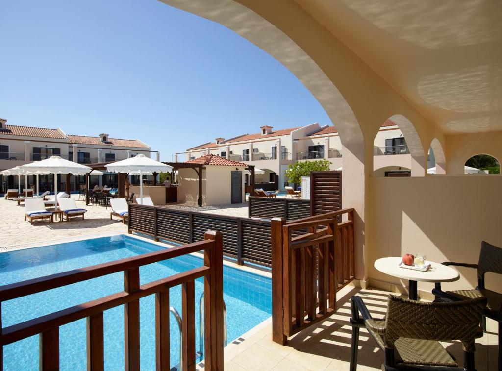 Balkons ar skatu uz peldbaseinu un atpūtas zonu viesnīcā, kur ir saulessargi un sauļošanās krēsli. Ideāla vieta relaksācijai un atpūtai saulainā dienā.