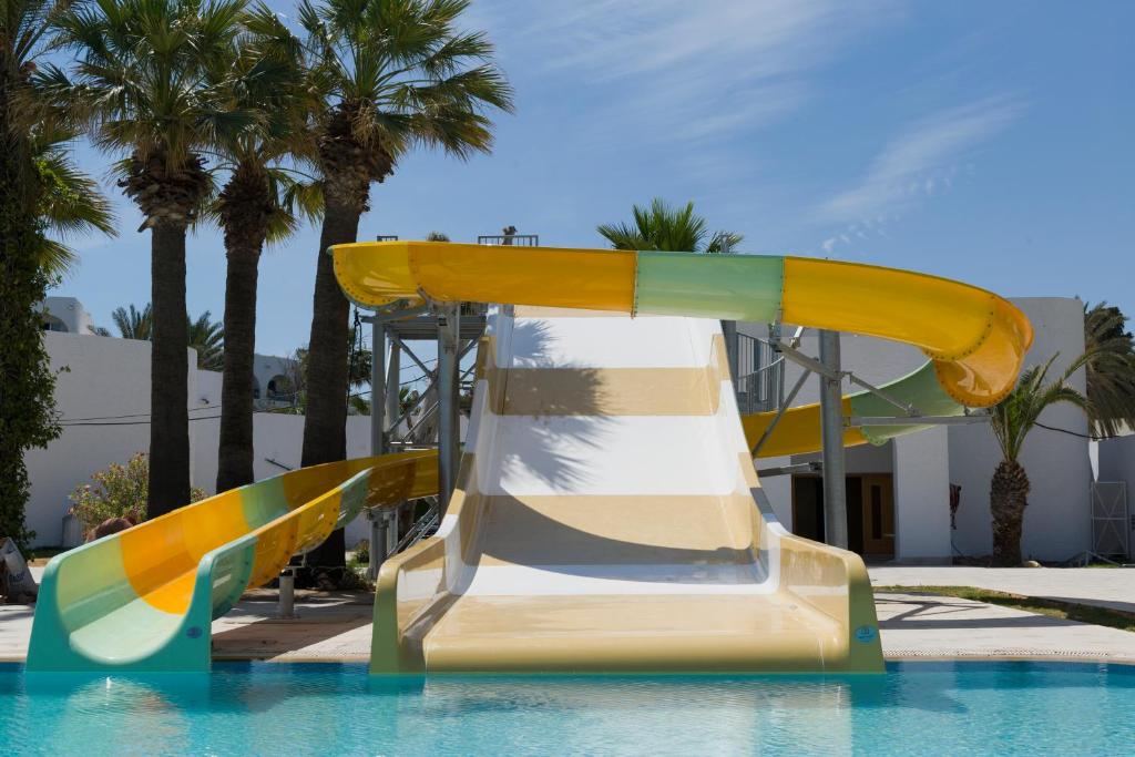 Ūdens slidkalniņš ar spilgtām krāsām atrodas pie peldbaseina, apkārt palmām un saulainam debesīm. Ideāla vieta atpūtai un izklaidei.